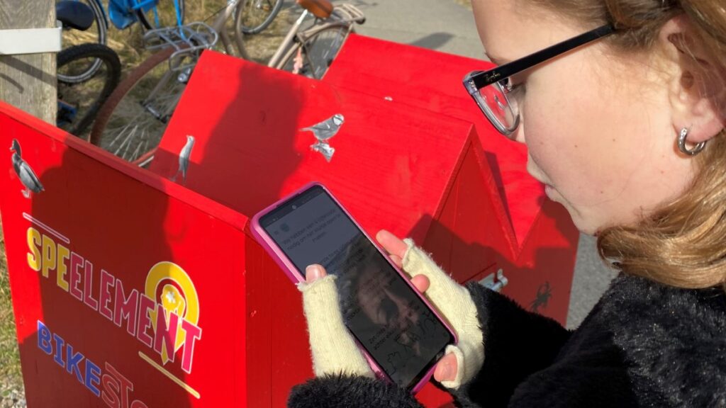 Een dame leest de tekst op haar telefoon voor de volgende aanwijzing bij Puzzelen op de Pedalen.